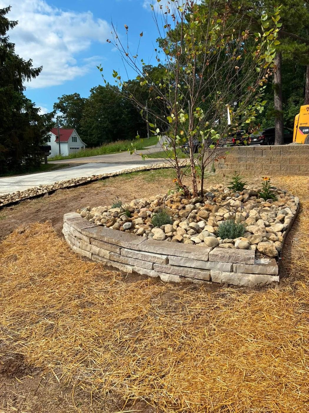 Stacked natural stone raised bed with river rock and a tree