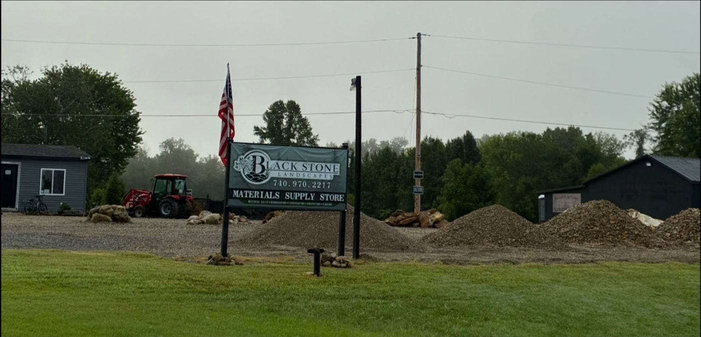 Black Stone Landscapes supply yard with stone piles and sign